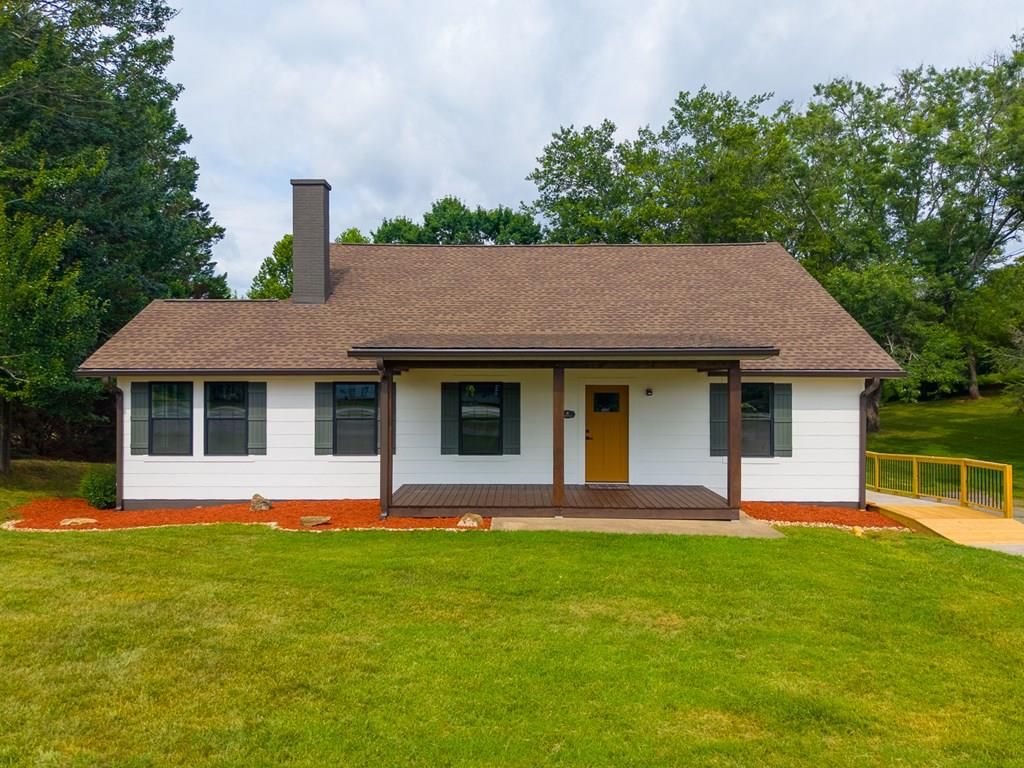 Front of the white cottage-style house with a covered front porch, mustard-yellow front door, and green shutters