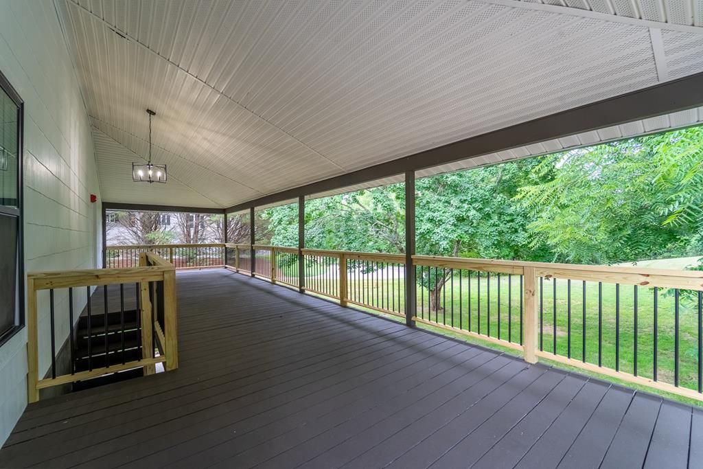 Covered back porch with a long deck and railing overlooking the yard